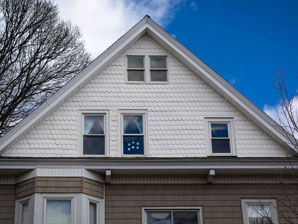 An upwards view of a home with scalloped siding on the second floor